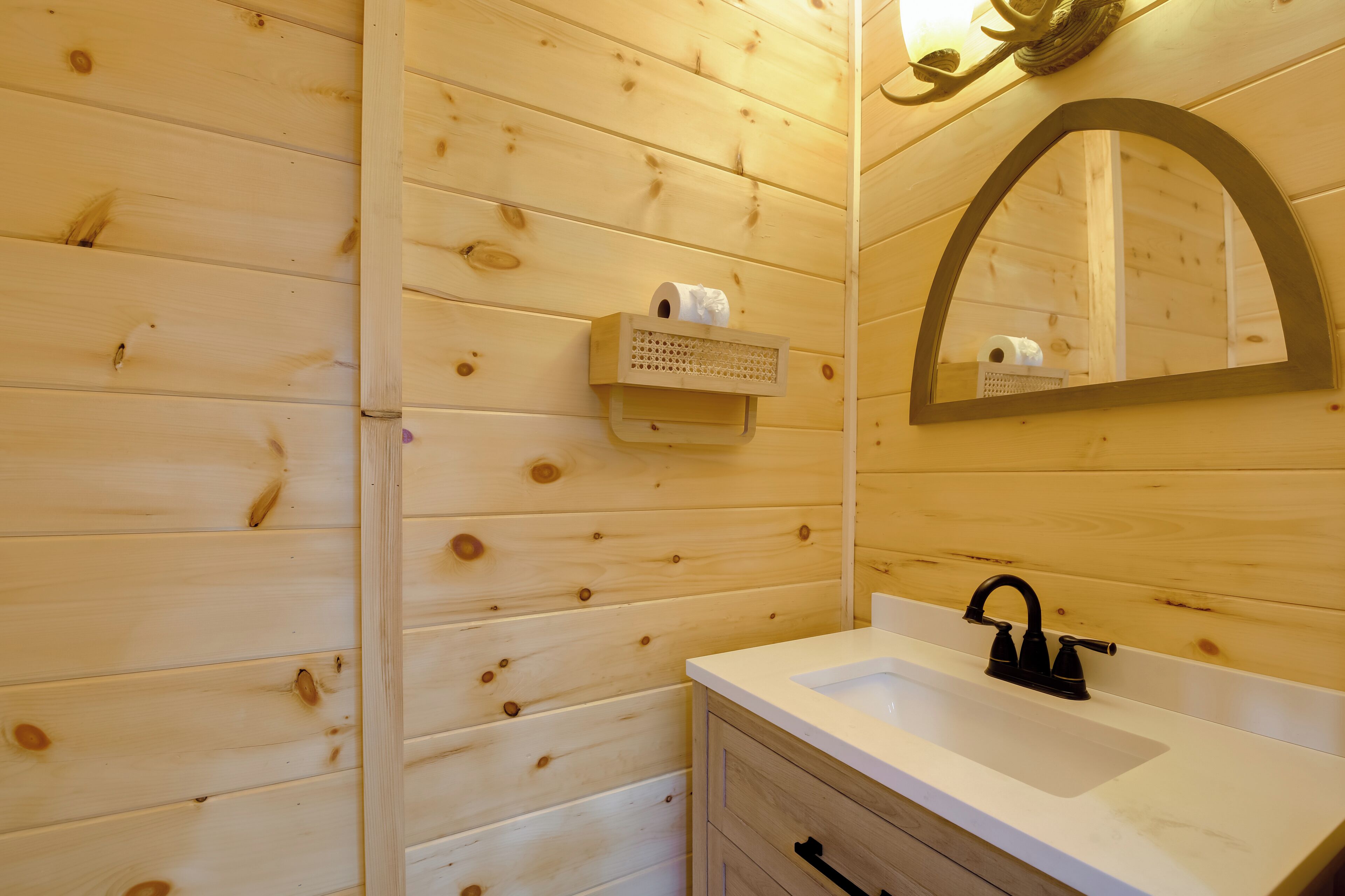 Ein Badezimmer einer Holzhütte mit Waschbecken, Spiegel und Toilettenpapierhalter.