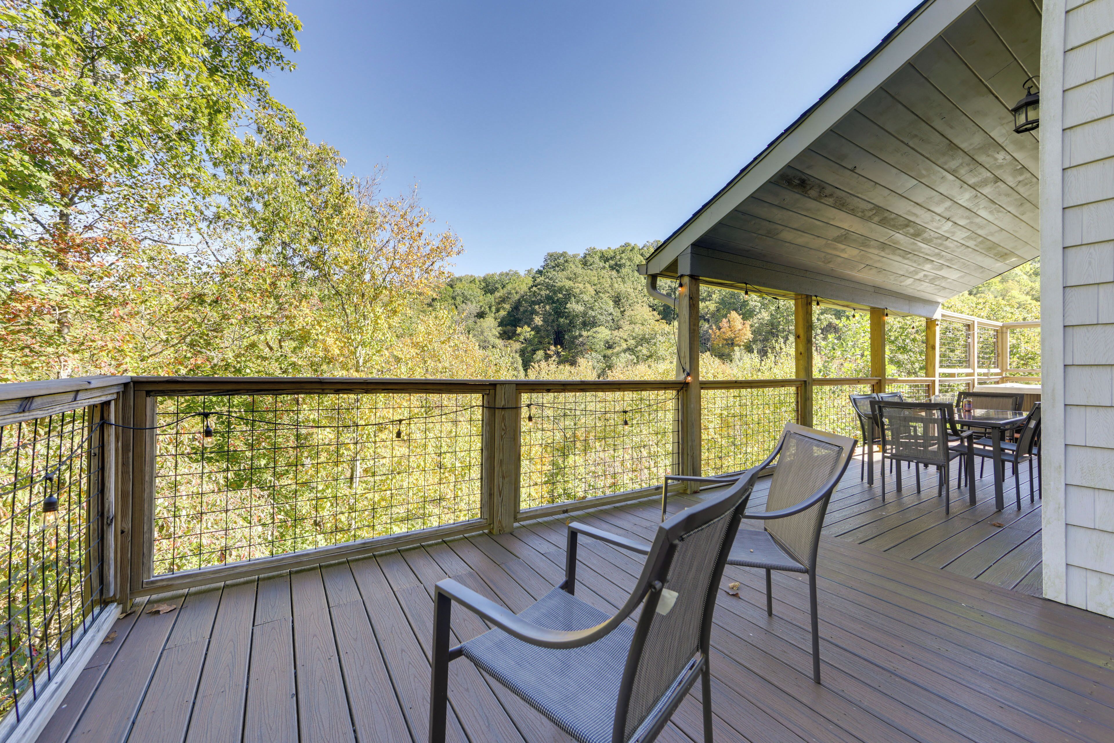 A wooden deck with a covered area, outdoor furniture, and a view of trees and foliage.