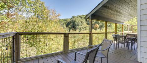 A wooden deck with a covered area, outdoor furniture, and a view of trees and foliage.