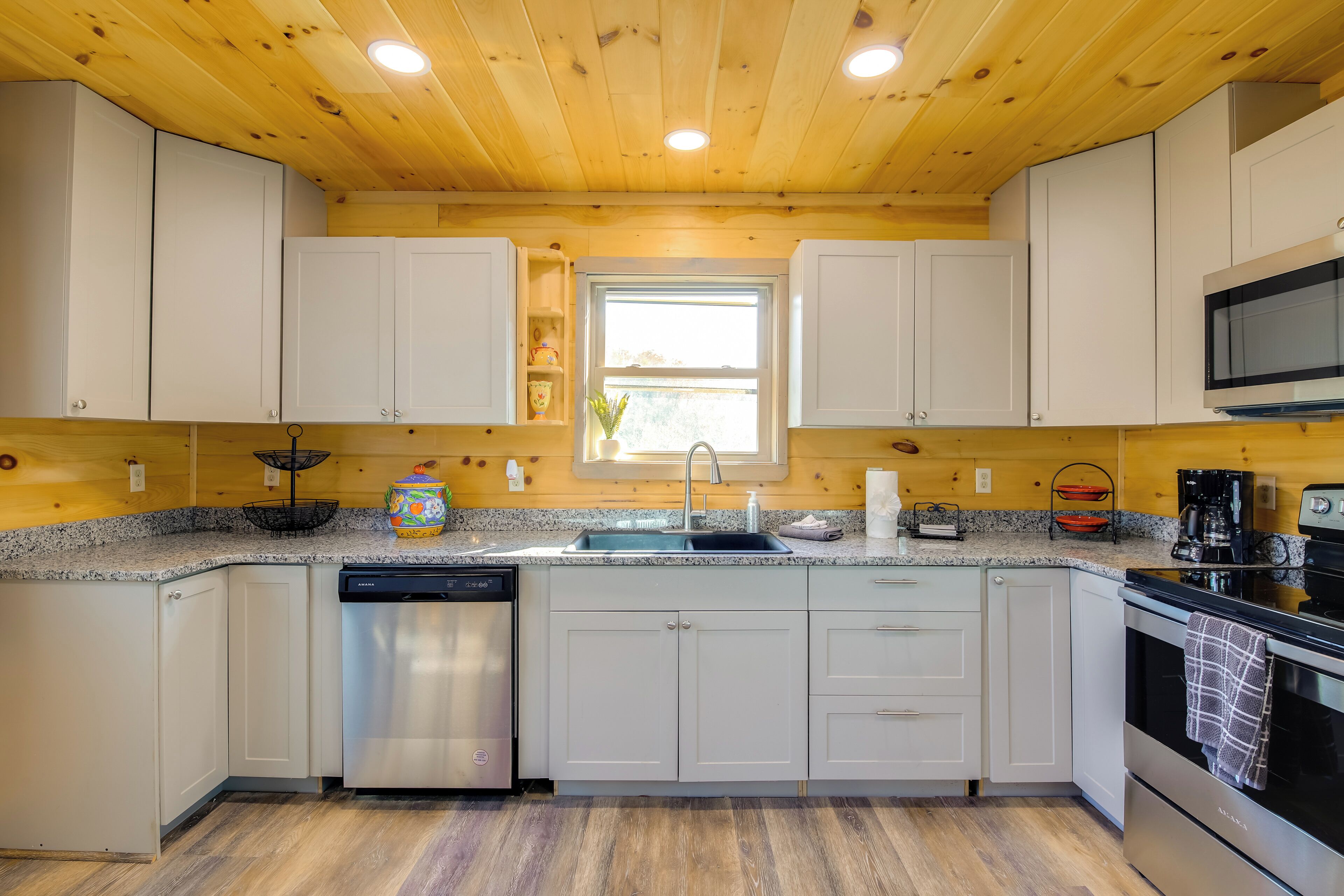 A modern kitchen with white cabinets, granite countertops, a dishwasher, a stove, and a microwave.