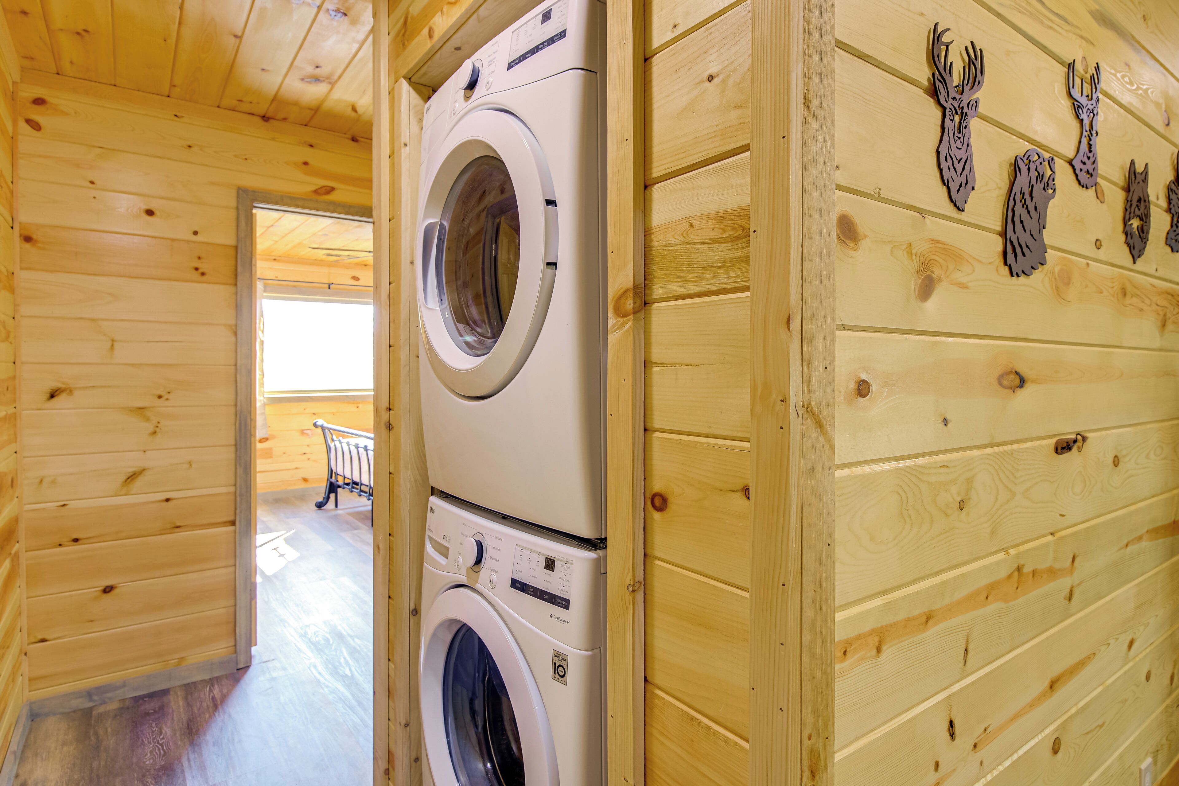 A laundry room with two stacked washing machines, wooden walls, and a bench in the background.