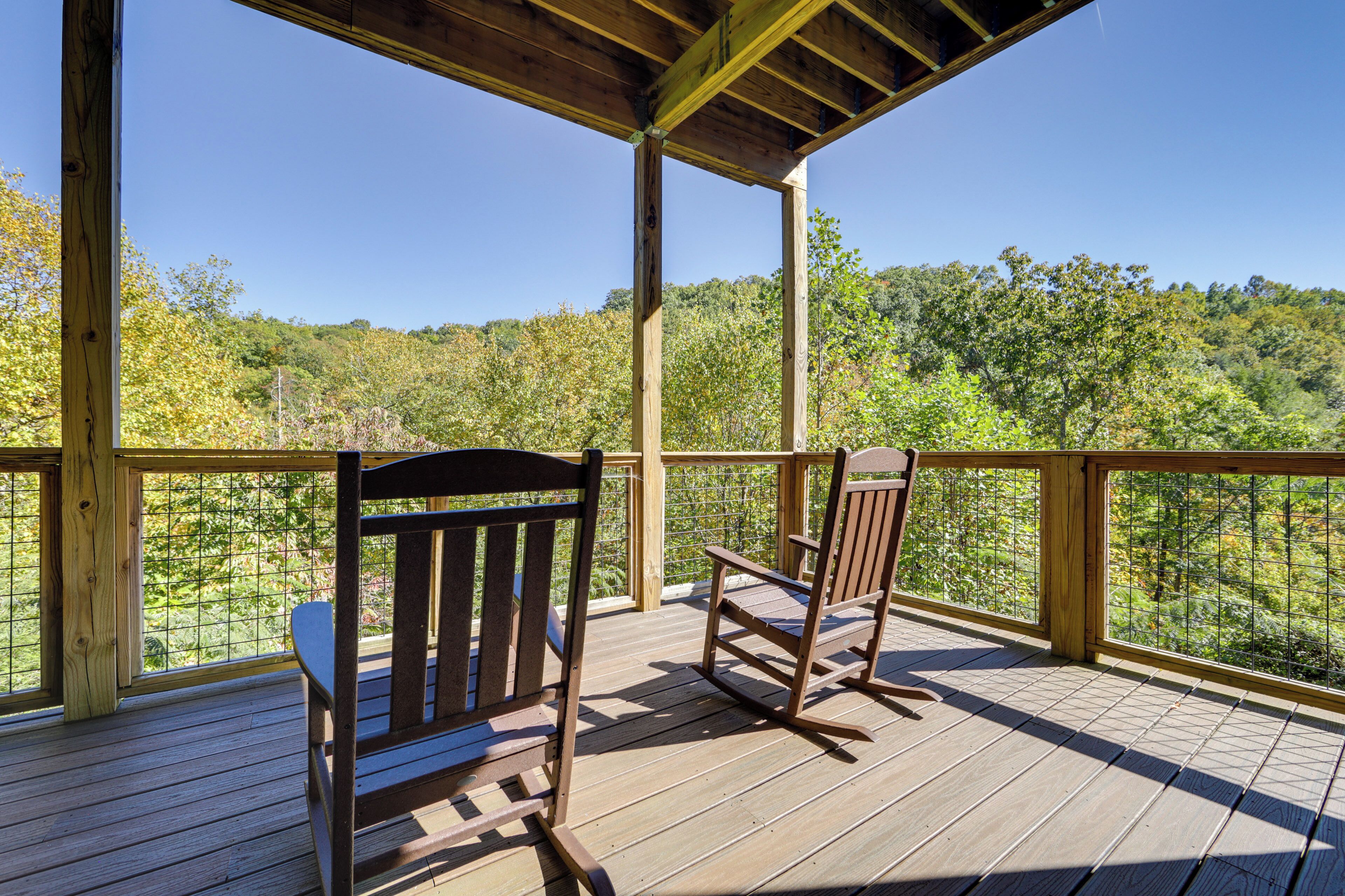Une terrasse en bois avec deux fauteuils à bascule donnant sur une colline boisée.