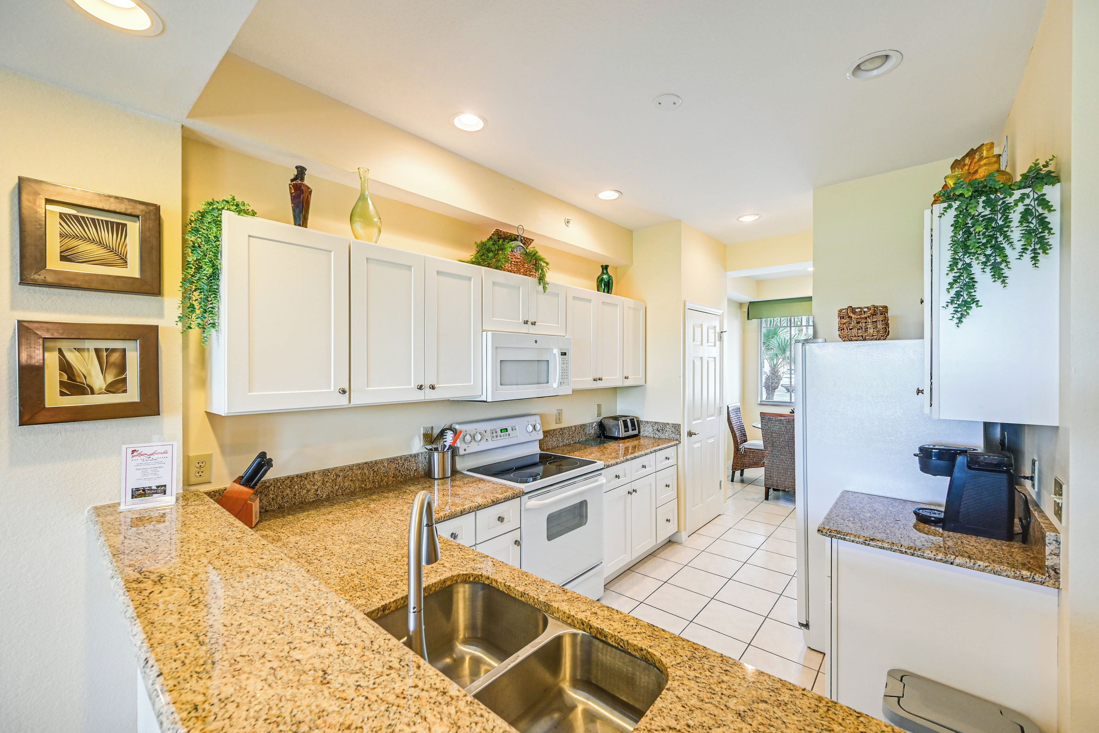 A modern kitchen with white cabinets, granite countertops, stainless steel appliances, and decorative plants.