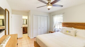 Une chambre à coucher comprenant un lit, un ventilateur de plafond, une tête de lit en bois, une table de chevet et un miroir.
