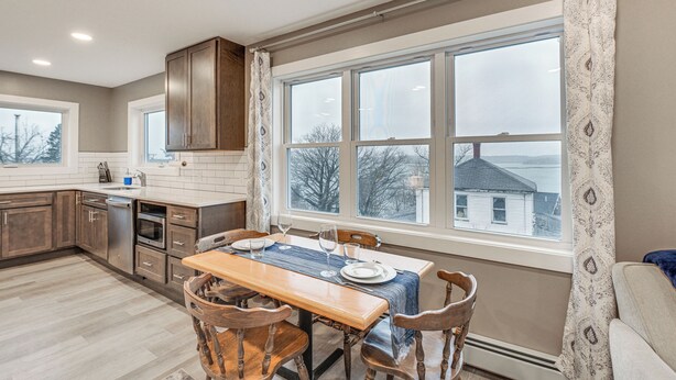 Una cocina con una mesa de comedor para cuatro personas, armarios de madera y un ventanal con vista a una casa.