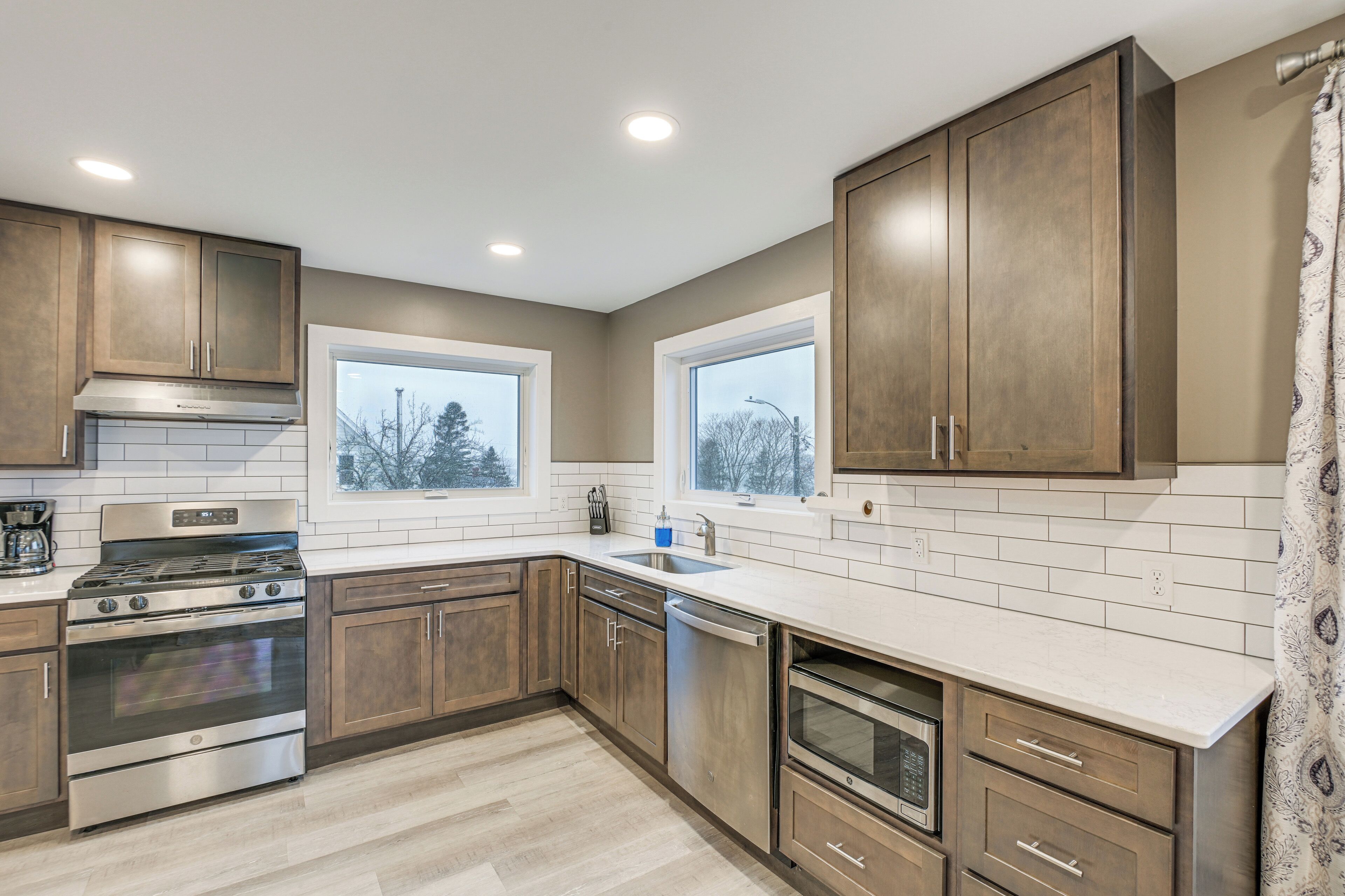 A modern kitchen with wooden cabinets, stainless steel appliances, and large windows.