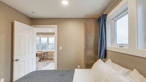 Un dormitorio con una cama, una ventana y una puerta que da a un comedor.