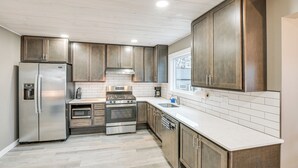 Cocina moderna con electrodomésticos de acero inoxidable, armarios de madera y salpicadero de azulejos blancos.
