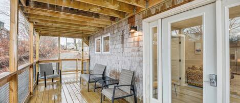 A covered porch with wooden beams, a glass door leading inside, and two chairs.
