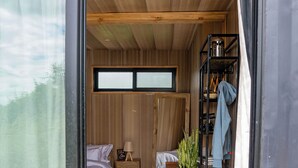 Un dormitorio con cama, mesita de noche, planta en maceta, estante con ropa y una ventana.