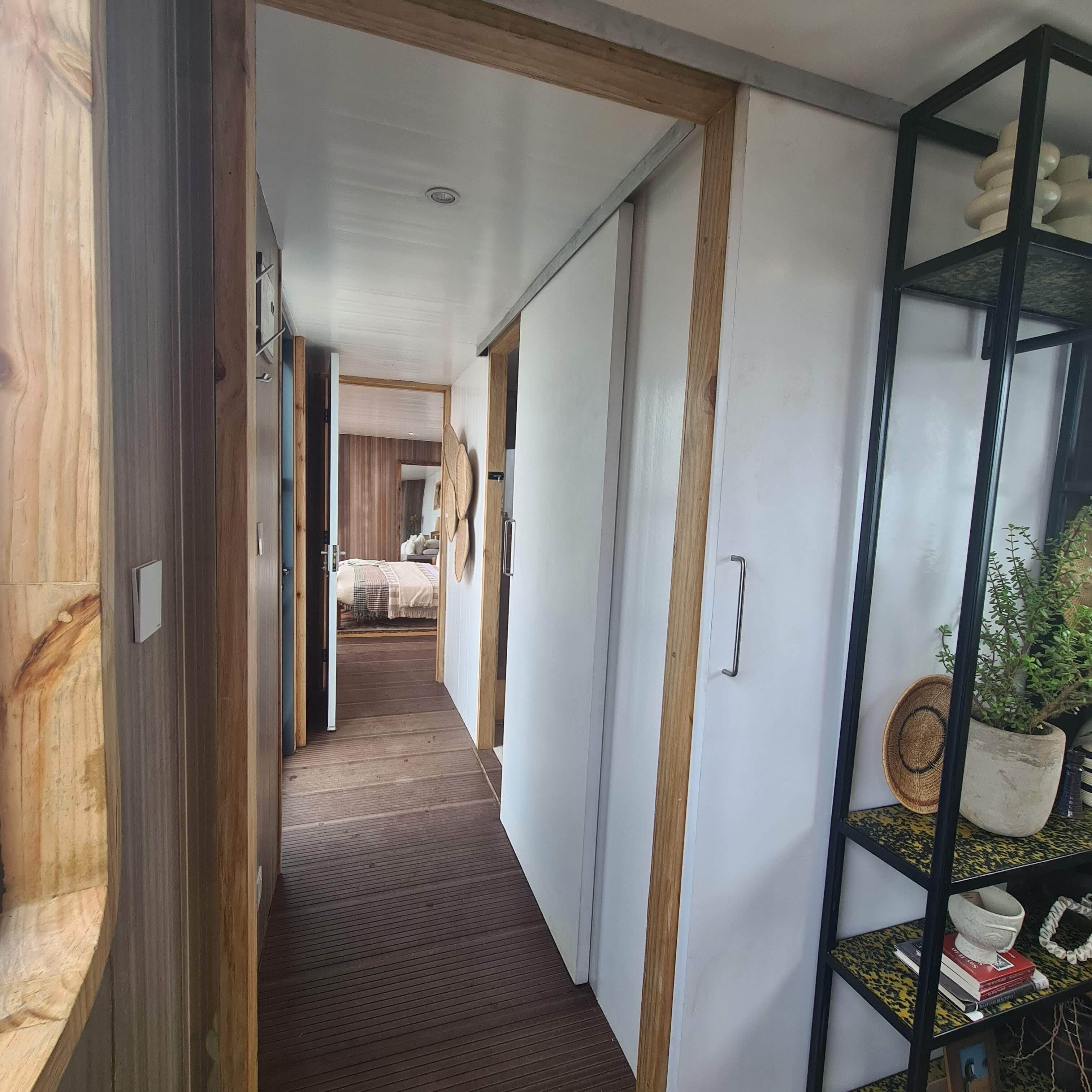 Un pasillo con piso de madera, una cama al fondo y una estantería con objetos decorativos.