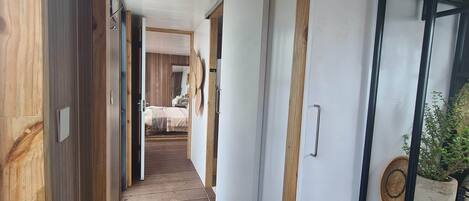 Un pasillo con piso de madera, una cama al fondo y una estantería con objetos decorativos.