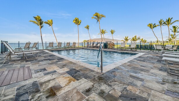 Zona de piscina con sillones de descanso y palmeras, con vistas a una masa de agua.