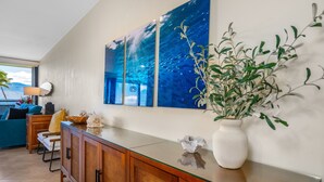 Una sala de estar moderna con una mesa de centro de vidrio, armarios de madera, un cuadro grande colgado en la pared y una planta en maceta.
