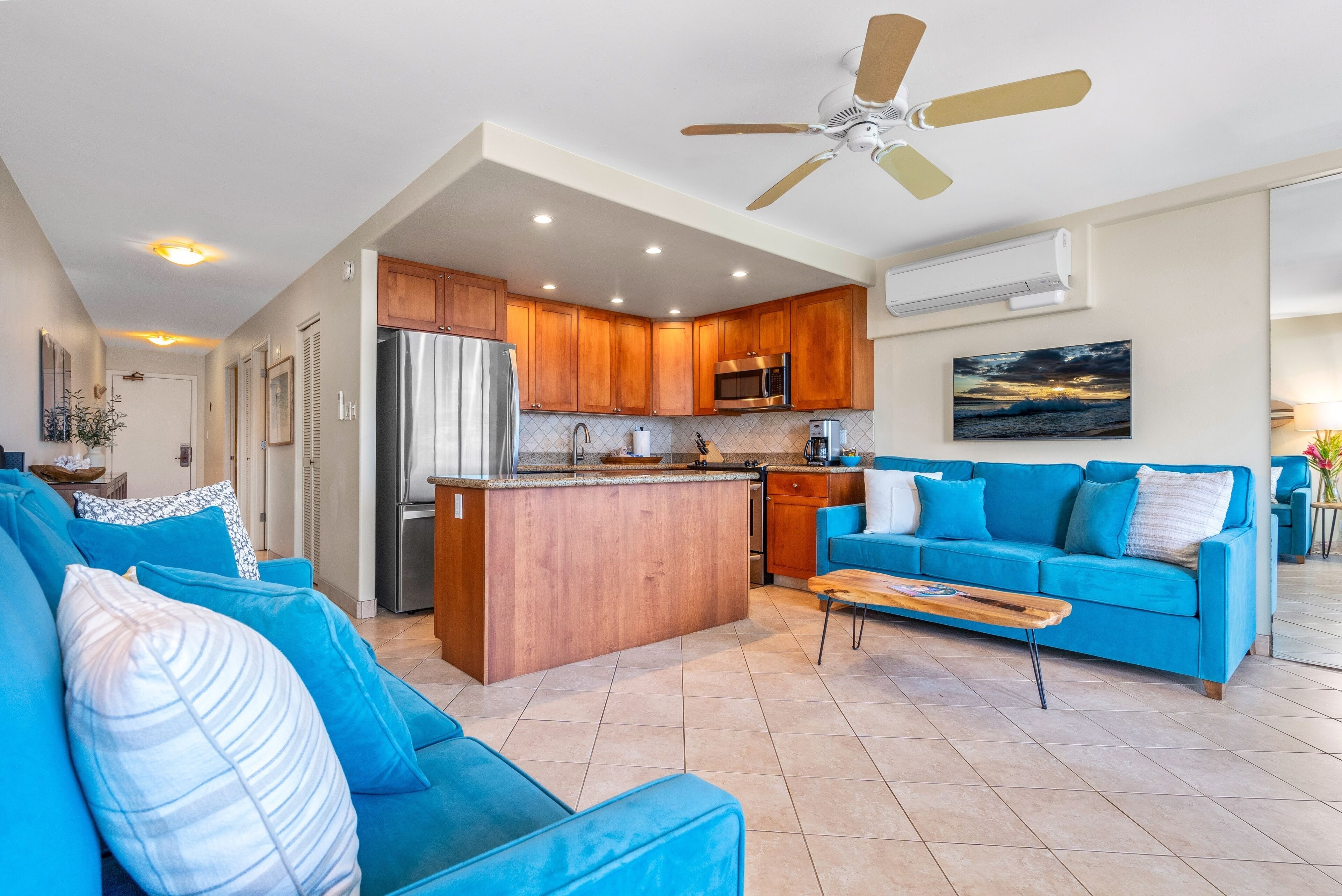Una sala de estar moderna con un sofá azul, una mesa de centro de madera y una cocina con gabinetes de madera y electrodomésticos de acero inoxidable.