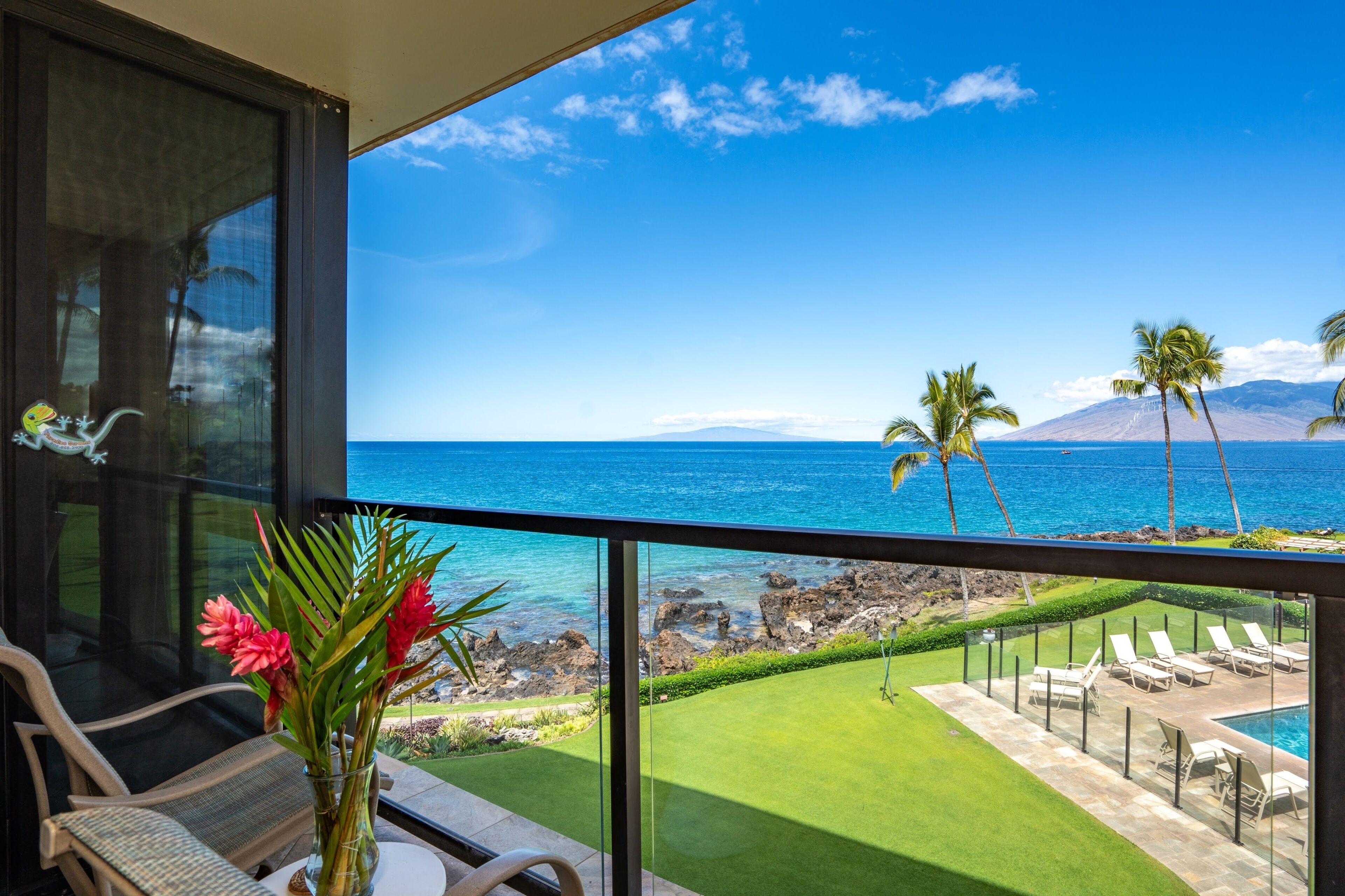 A balcony with a view of the ocean, a pool, and lounge chairs.