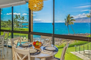 Un comedor con una mesa dispuesta para dos, con vistas a un paisaje marino con palmeras y cielo despejado.