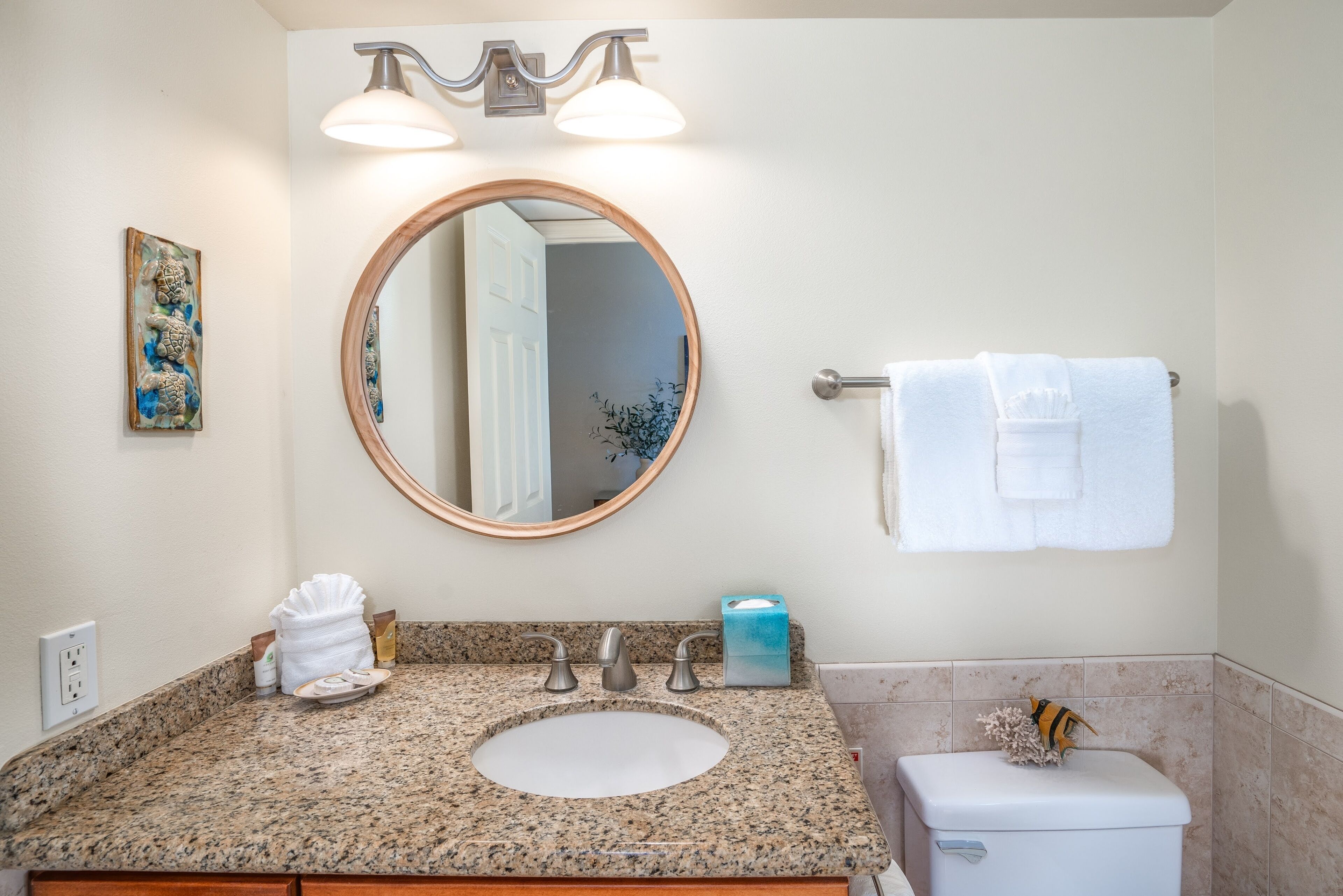 A bathroom with a granite countertop, a round mirror, a towel rack, and a toilet.