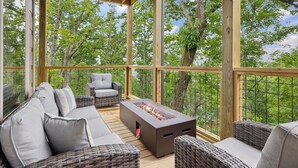 A covered outdoor seating area with wicker furniture and a built-in fire feature. - Tennessee Whiskey 3 Bedroom Cabin by RedAwning (Sevierville)