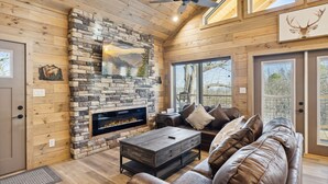 A cozy log cabin interior with a stone fireplace, leather sofa, and large windows. - Tennessee Whiskey 3 Bedroom Cabin by RedAwning (Sevierville)