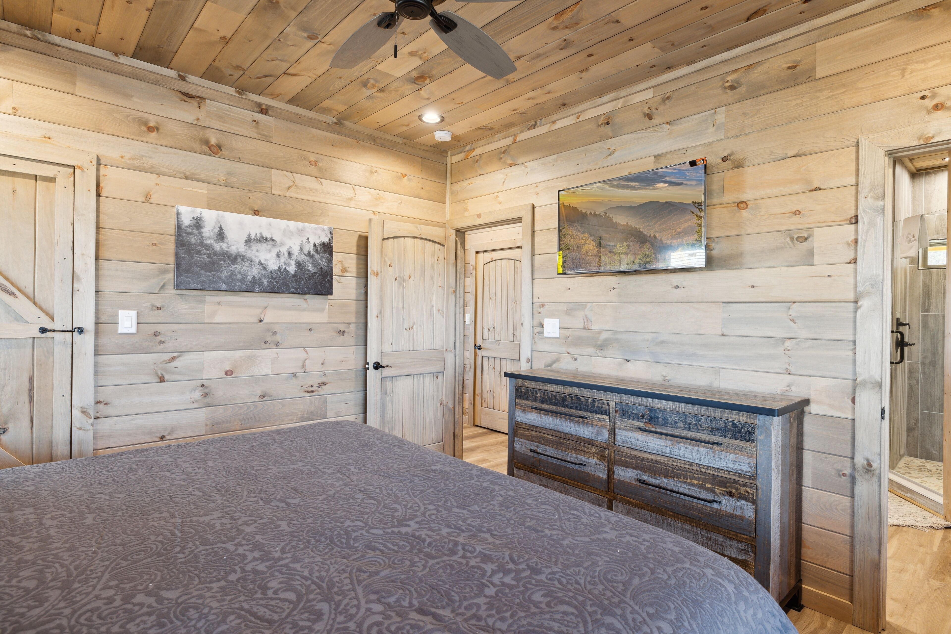 A wooden-paneled room with a bed, a dresser, and a ceiling fan.