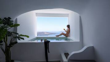 Una mujer sentada junto a una ventana con vista a una piscina y al mar.