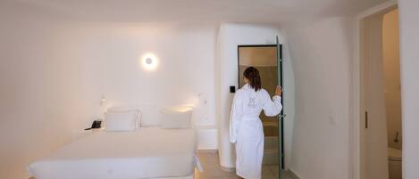 Une chambre à coucher comprenant un lit, une table de chevet, une lampe fixée au mur et une porte donnant sur une autre pièce.