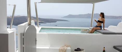 Piscina privada al aire libre con vista al mar, una silla de descanso, una mesa pequeña con una botella y un vaso, y un cesto con toallas.