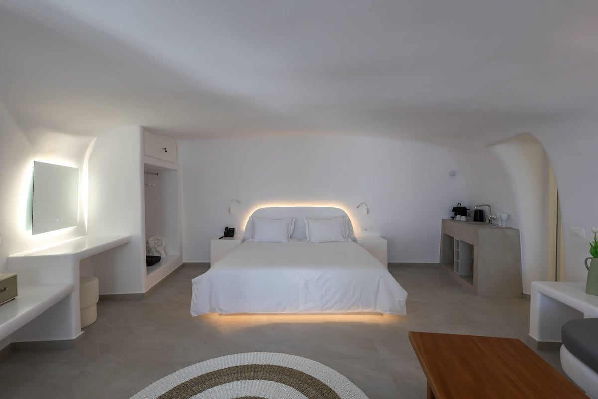 A minimalist bedroom with a large bed, bedside tables, a built-in bench, and a wall-mounted mirror.