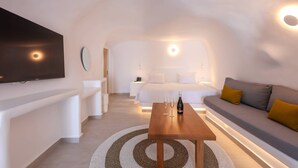 Una habitación de hotel moderna con televisión, cama, sofá y una mesa con vasos y una botella.