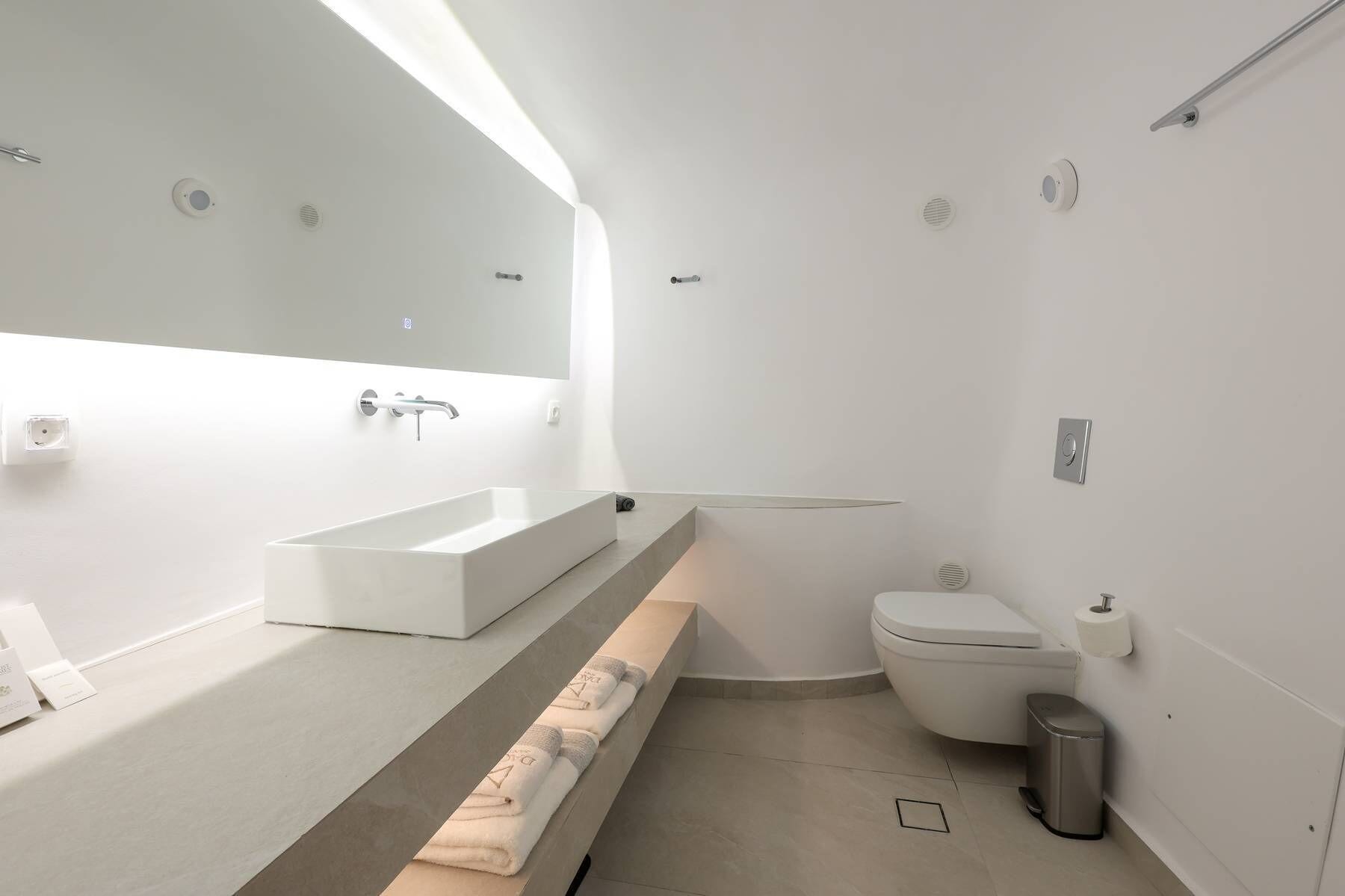 Un baño moderno con un lavamanos blanco grande, un espejo, un inodoro y un cubo de basura.