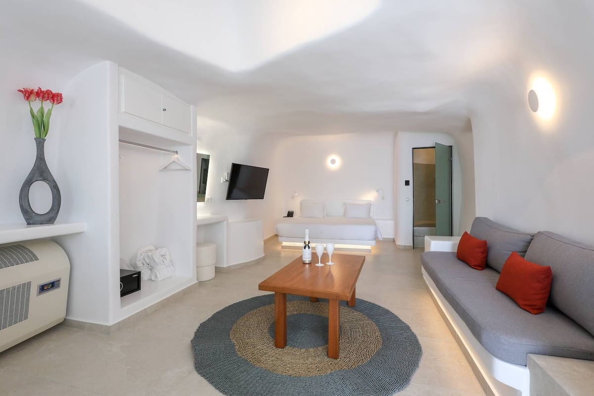 A modern living room with a sofa, a coffee table, a TV mounted on the wall, a bed, and a walk-in closet.