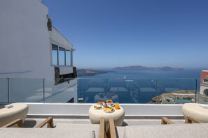 A balcony with a table set for breakfast overlooking the sea. - Dagaz Suites (Santorini)
