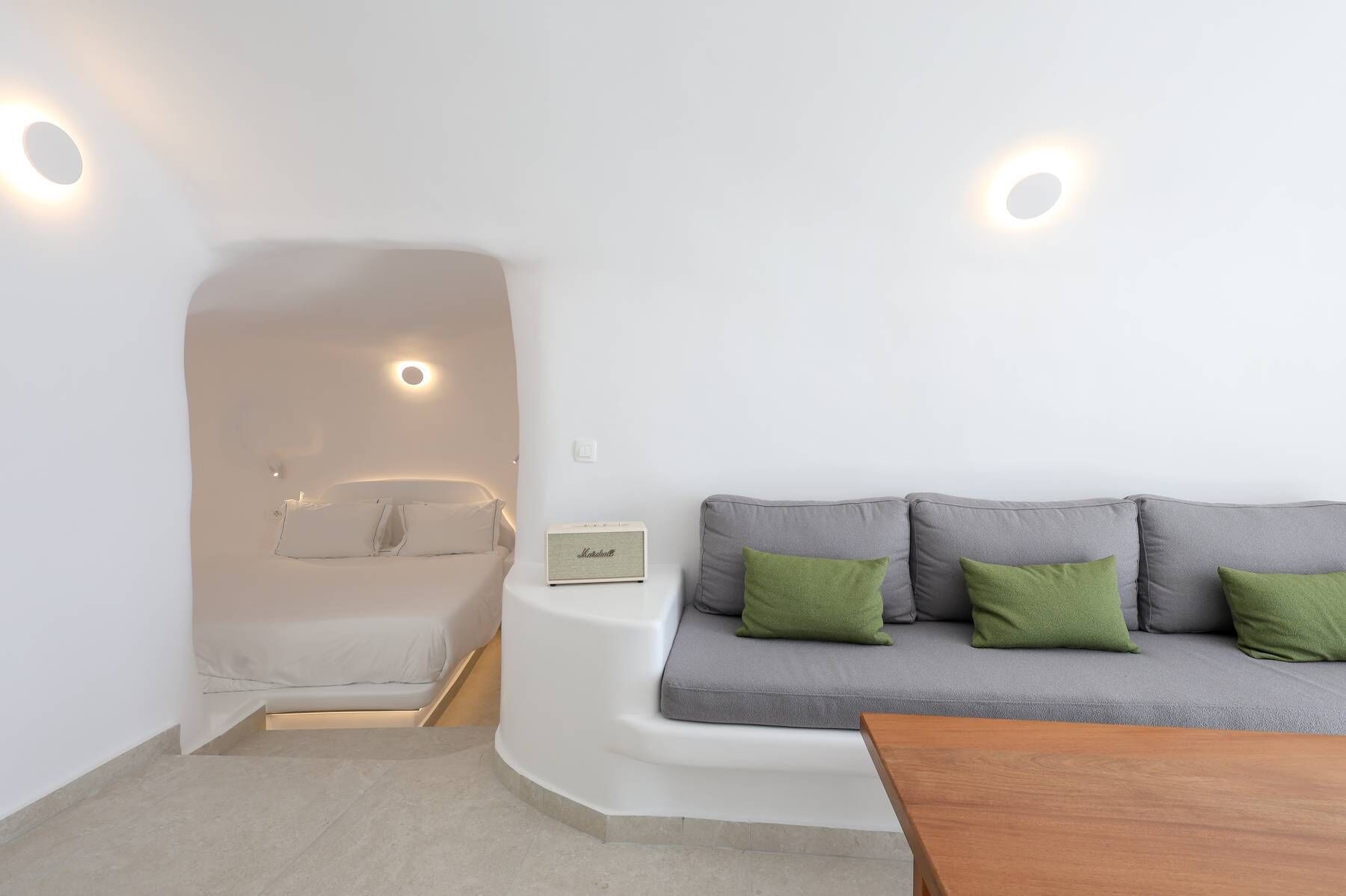 A modern room with a built-in bathtub, a grey sofa with green cushions, and a wooden table.