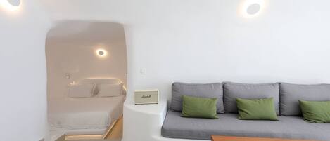 A modern room with a built-in bathtub, a grey sofa with green cushions, and a wooden table.
