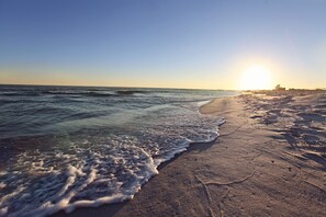 A beach with waves, a clear sky, and the sun setting or rising.