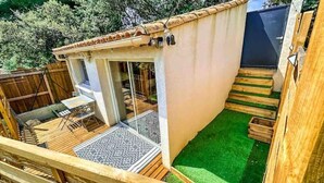 Ein kleiner Patio-Bereich mit Holzdeck, einem gemusterten Teppich und synthetischem Rasen.