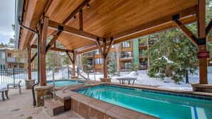 Piscina exterior techada con jacuzzi, rodeada por una terraza de madera y suelo cubierto de nieve.