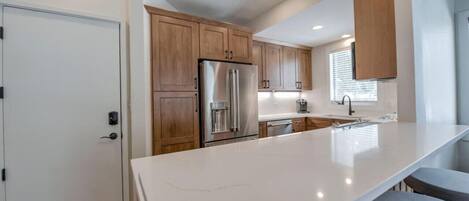 A modern kitchen with wooden cabinets, a stainless steel refrigerator, and a large marble countertop.