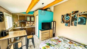 Une pièce compacte comprenant un coin cuisine, un lit avec une literie à motifs floraux et un mur orné d’œuvres d’art abstraites.