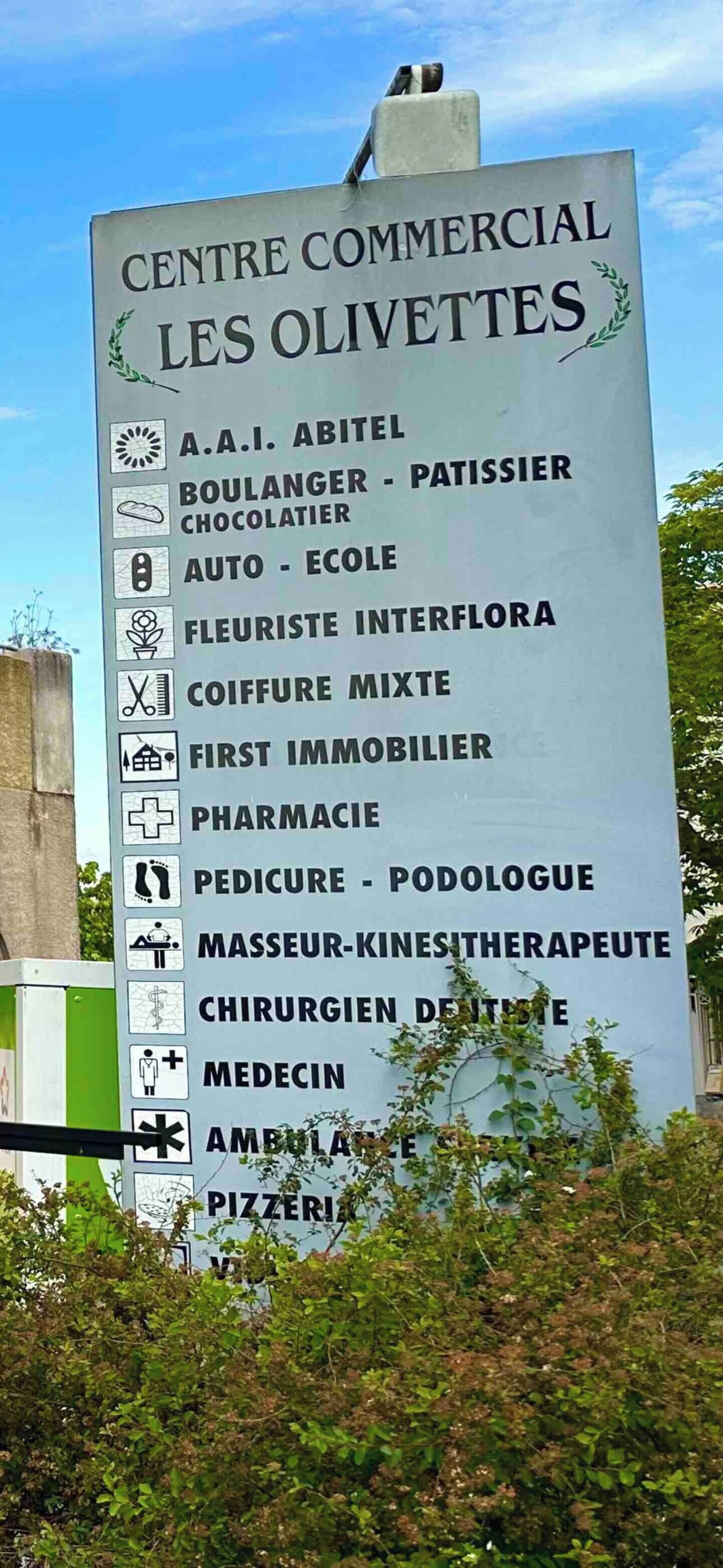 Een bord met een overzicht van diverse voorzieningen, zoals een bakkerij, apotheek en medische faciliteiten bij Centre Commercial Les Olivettes.