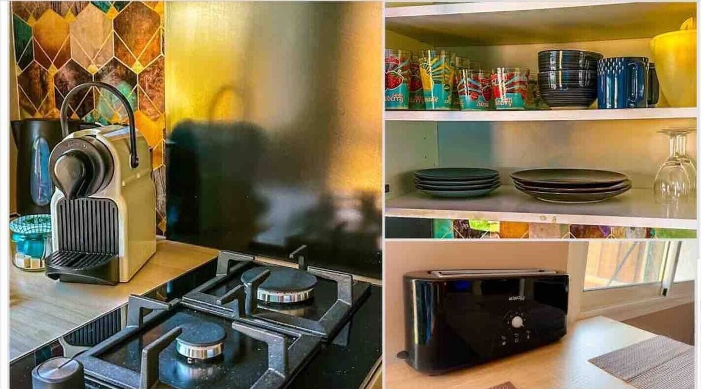 Una cocina con estufa a gas, tostadora y microondas. Hay repisas con platos, tazones y vasos.