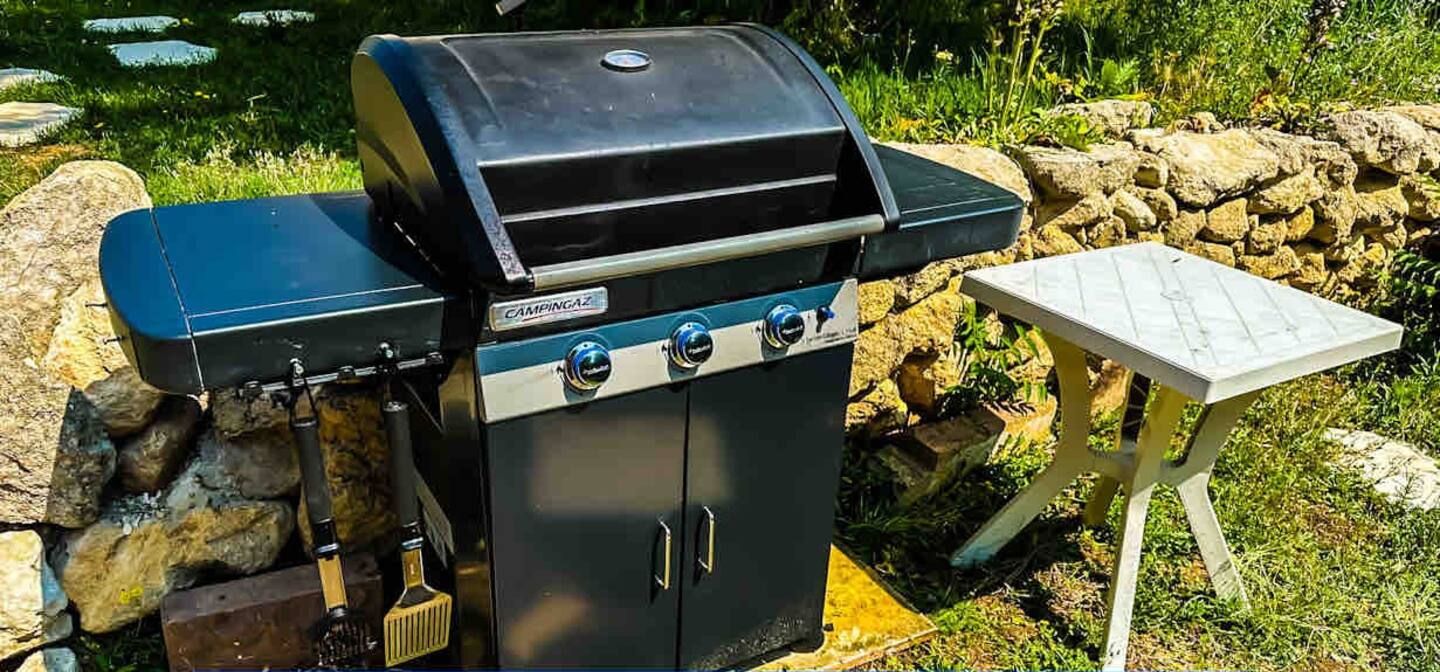 A black barbecue grill with a gas option, a small table, and a stone wall in the background.