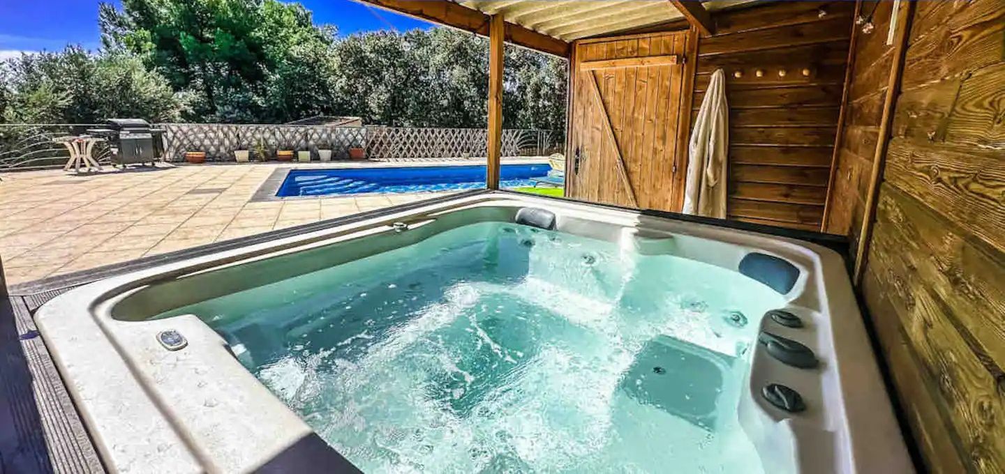 Un jacuzzi con una terraza de madera y una piscina al fondo.