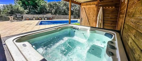 A hot tub with a wooden deck and a pool in the background.