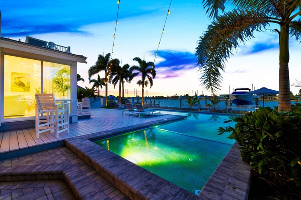 A modern hotel with a swimming pool, lounge chairs, and palm trees.