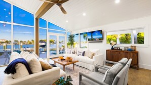 A modern living room with a large window overlooking a marina, a ceiling fan, and a bar area with a sign.
