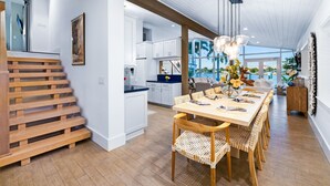 A modern kitchen with white cabinets, a wooden staircase, and a dining area with a long table and wicker chairs.