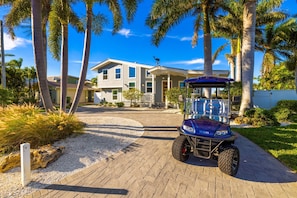 A golf cart parked in front of a two-story house with a driveway leading to the entrance.