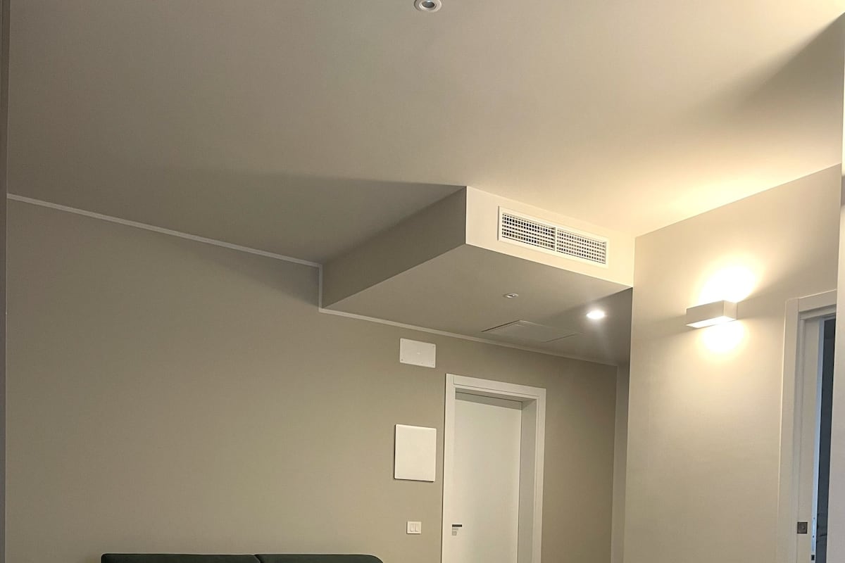 A bedroom with a large bed, a dark green sofa, a white door, and a light switch on the wall.